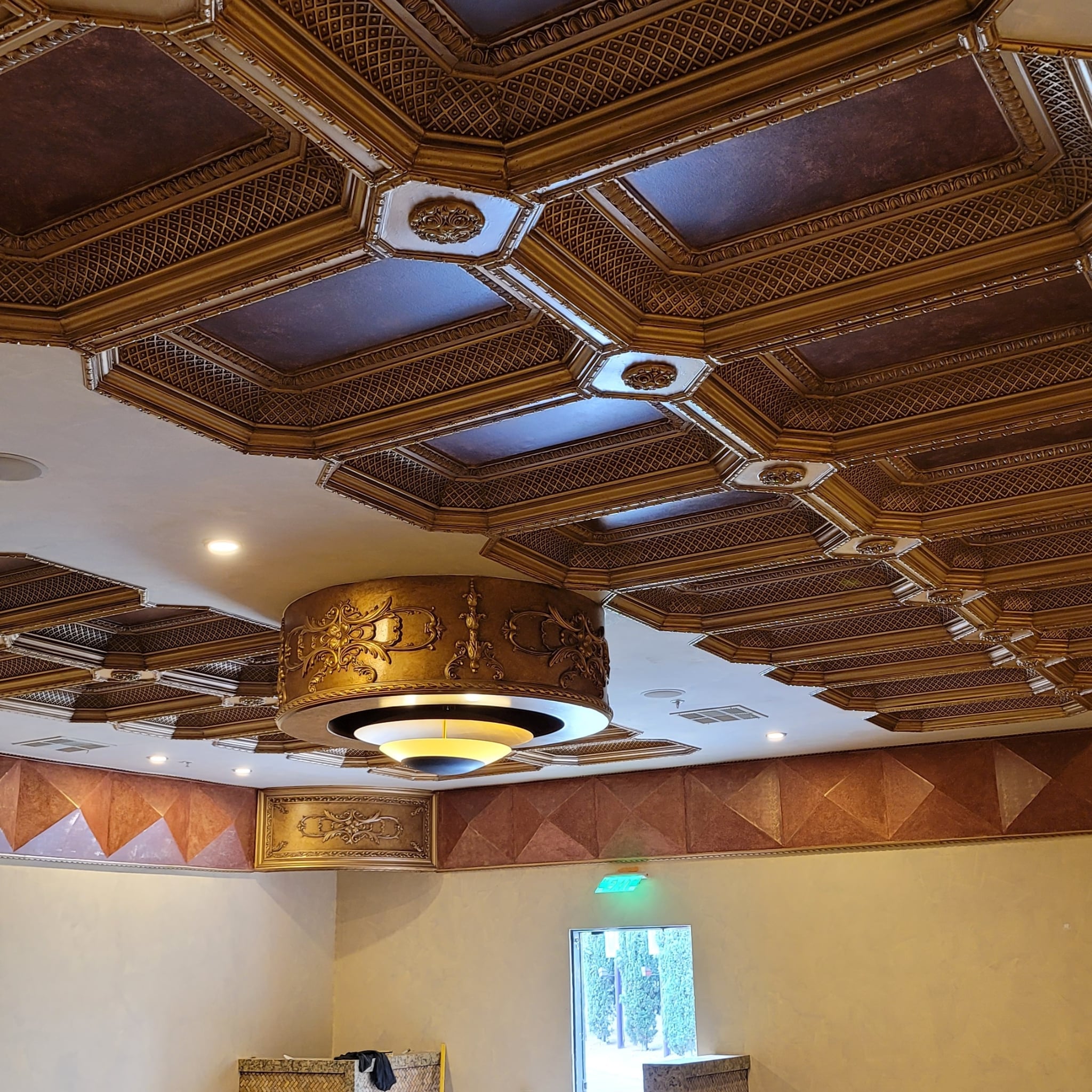 Decorative ceiling with intricate patterns and a chandelier in an indoor setting.